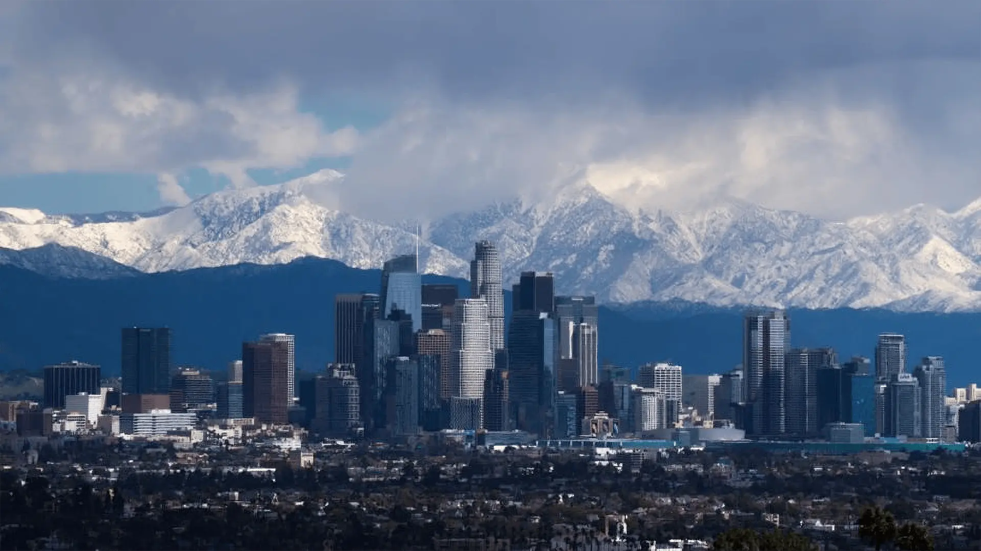 An image of the snow-capped mountains bordering the Los Angeles basin, seen under a clear blue sky dotted with white clouds. The wet streets reflect the morning light, symbolizing the cleansing power of rain, and a distant path leads towards a hidden valley, representing the spiritual journey described in the article. by Ted Tschopp